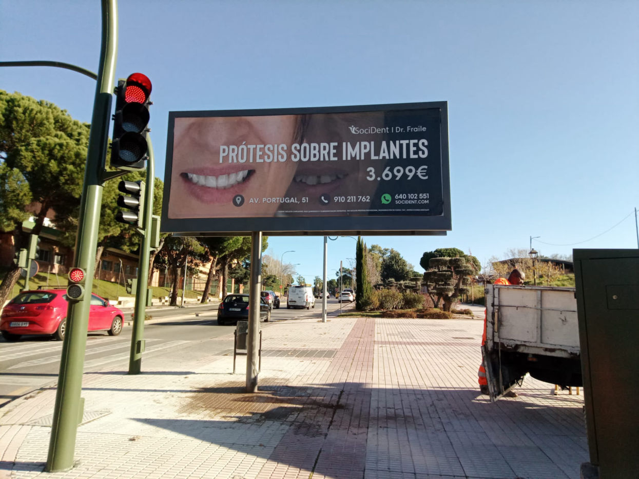 Cartel publicitario en vía urbana, promocionando servicios de prótesis sobre implantes con alta visibilidad para peatones y conductores.